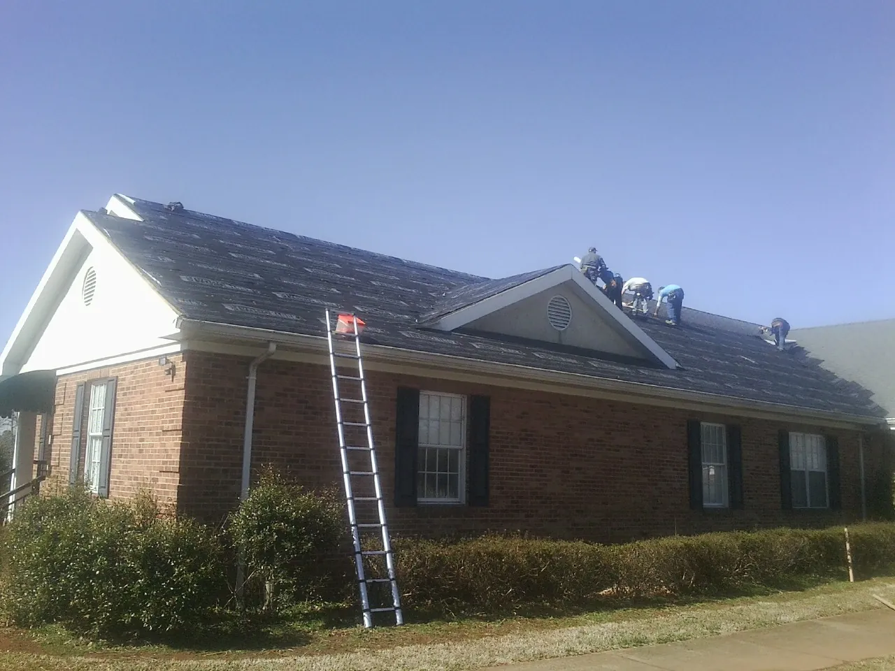Crew tearing shingles off a brick ranch roof with a ladder set — Emergency Roof Repair work by our crew in Fish Haven