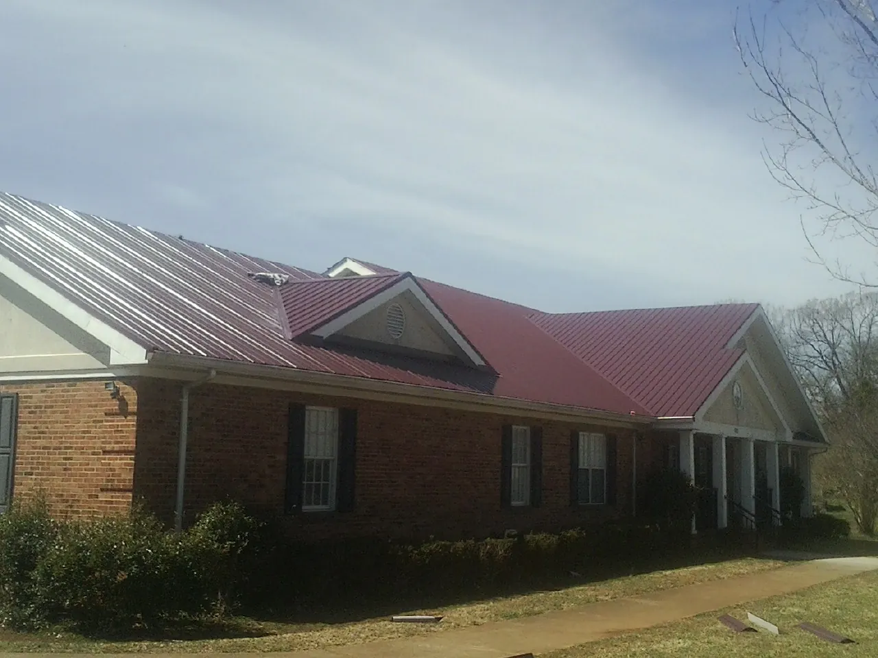 Red metal roof with gabled entries on a long brick building, from a Hail Damage Roof Repair job in Fish Haven