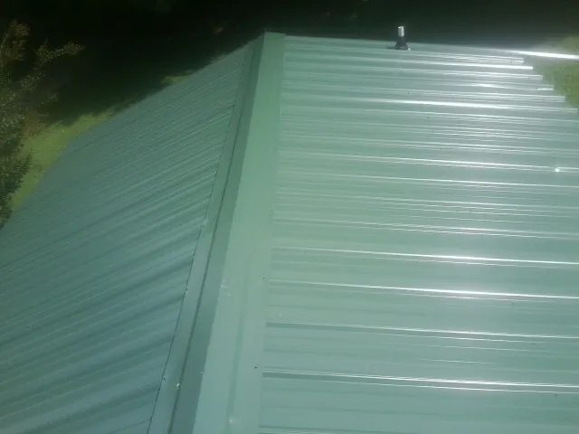 New green metal panels meeting at the ridge of a roof — Flat Roof Repair work by our crew in Fish Haven