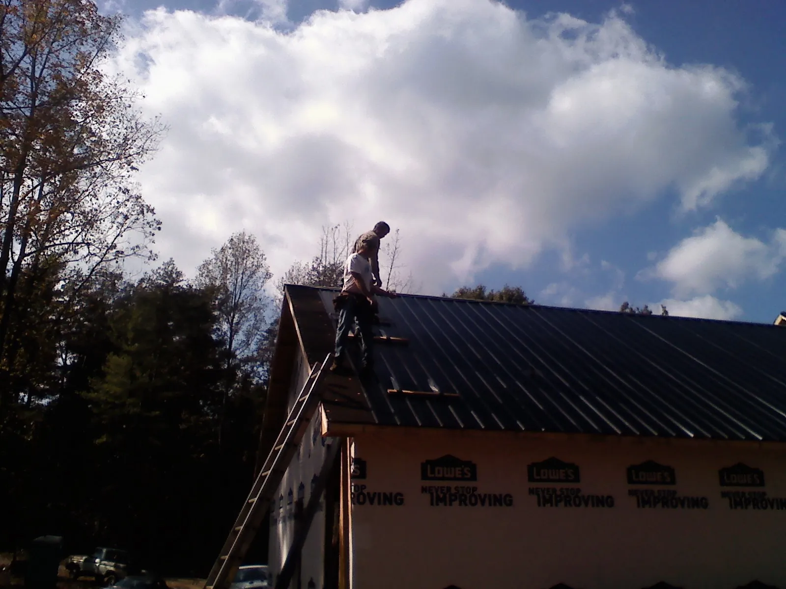 Roofer fastening dark metal panels high against a cloudy sky, from a Roof Inspection job in Fish Haven