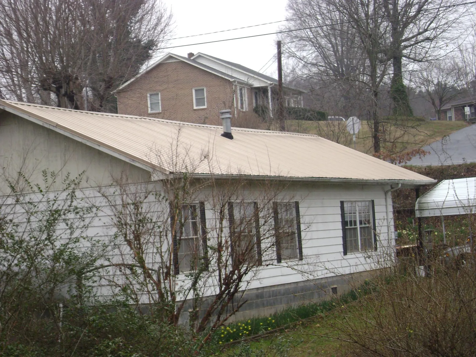 Tan metal roof on a white sided house set into a hillside — Commercial Roofing by Roofing Brothers in Fish Haven