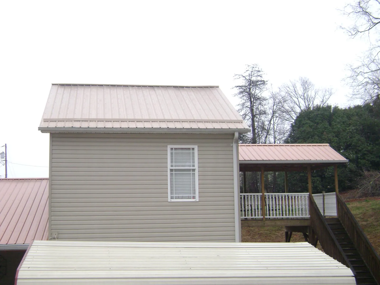Tan metal roofs on a two story addition and attached porch, from a Roof Replacement job in Fish Haven